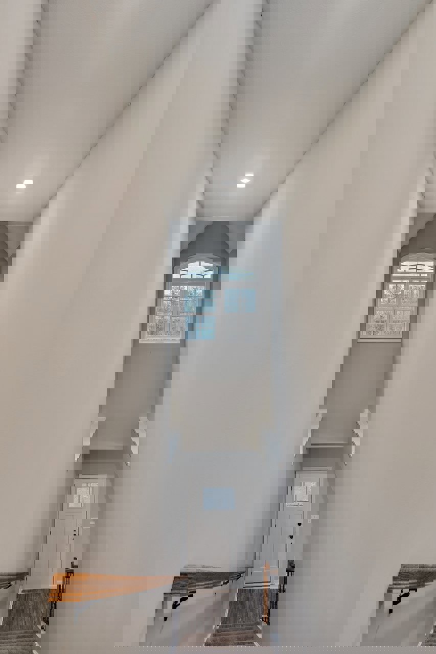 Hallway with light wood flooring, white plaster walls, white-framed window, white door, wooden shelf, and staircase with wood treads