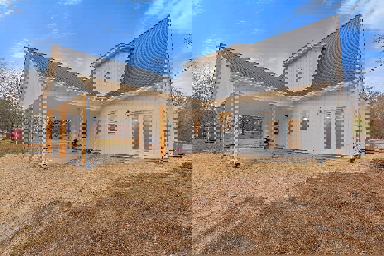 White house with covered patio, large windows, manicured lawn, and mature trees in the background