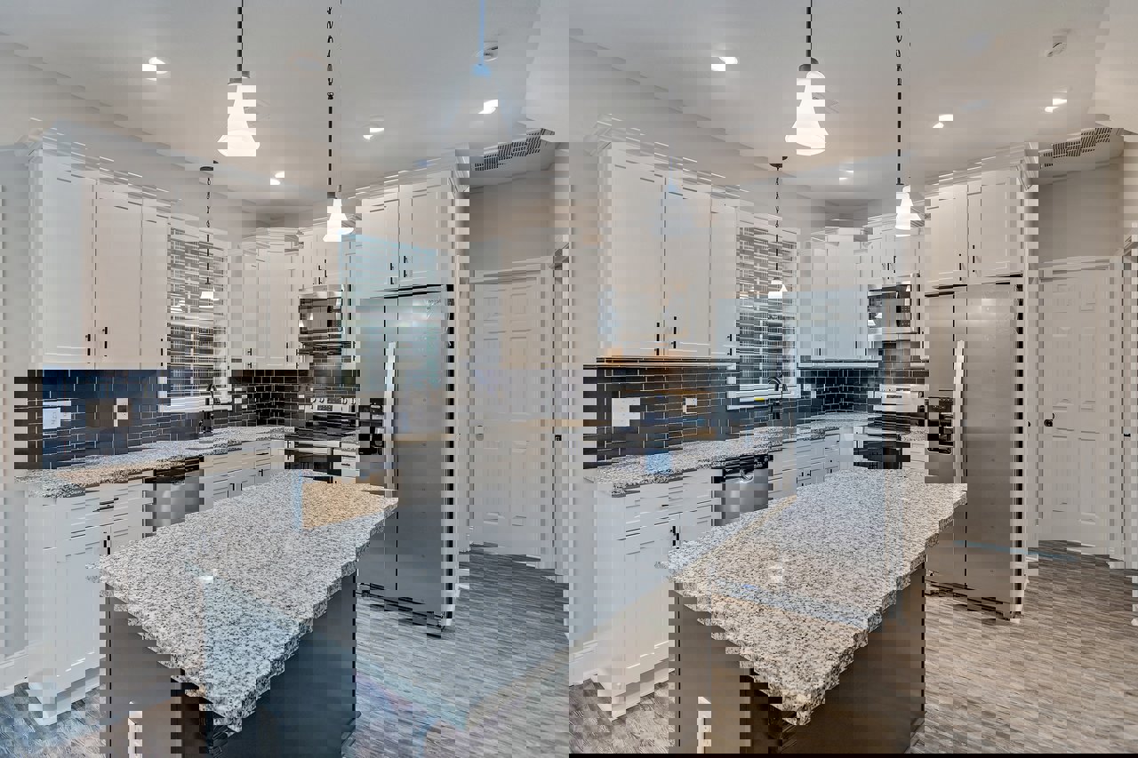 Granite island with undermount sink, stainless steel refrigerator and microwave, white cabinetry, pendant light fixtures, and neutral tile backsplash