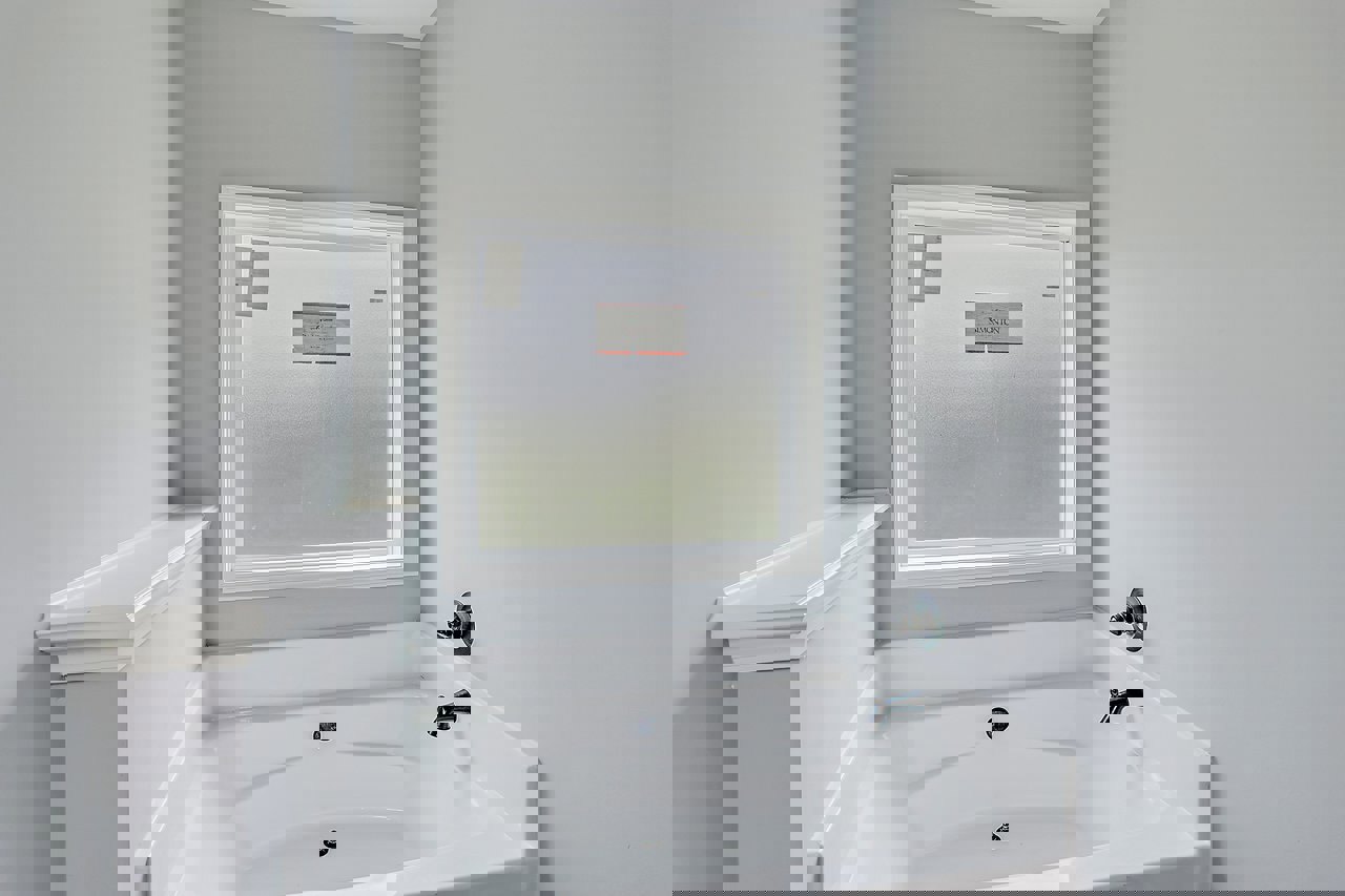 Freestanding white bathtub with chrome faucet and drain, positioned beneath a window displaying a sign with black text, surrounded by light-colored bathroom walls