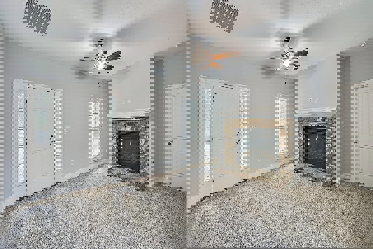 Living room with brick fireplace featuring glass doors, ceiling fan with light fixture, white-framed window, and vent on white ceiling