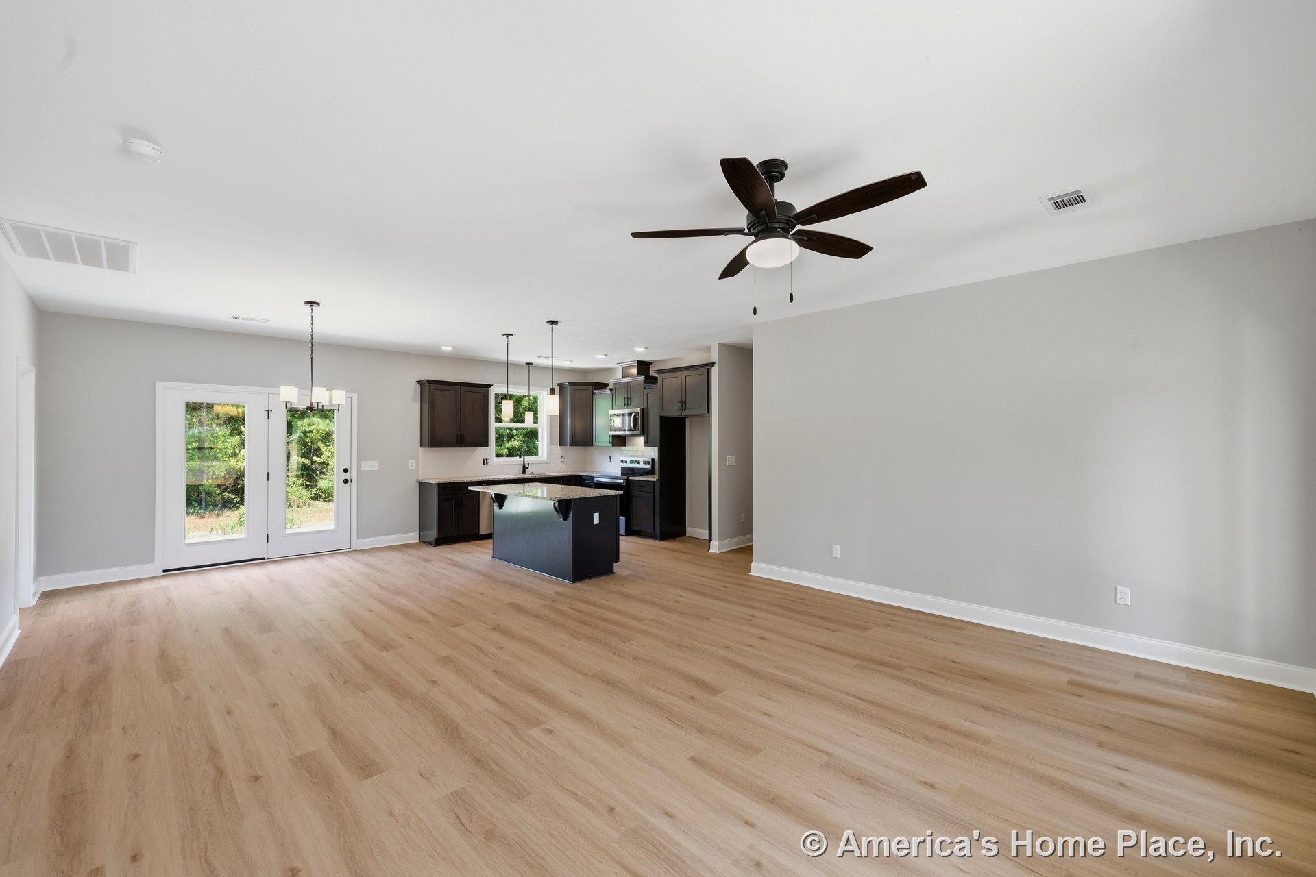 Open concept living area with light wood plank flooring, ceiling fan with light, kitchen featuring dark cabinets, granite central island, pendant and chandelier lighting, and