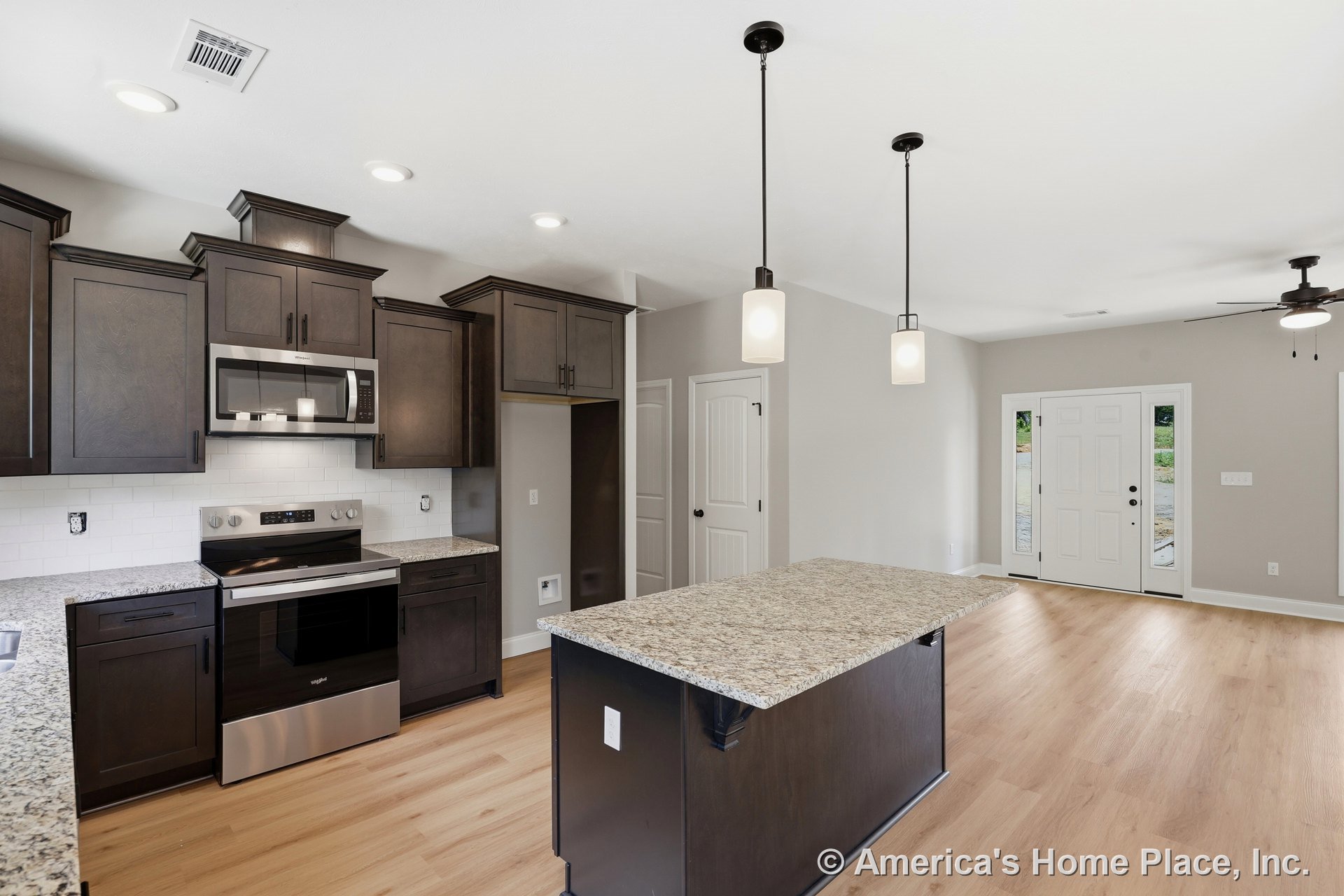 Dark wood kitchen cabinetry, granite countertops, central island with pendant lights, stainless steel oven and microwave, white subway tile backsplash, recessed ceiling lights