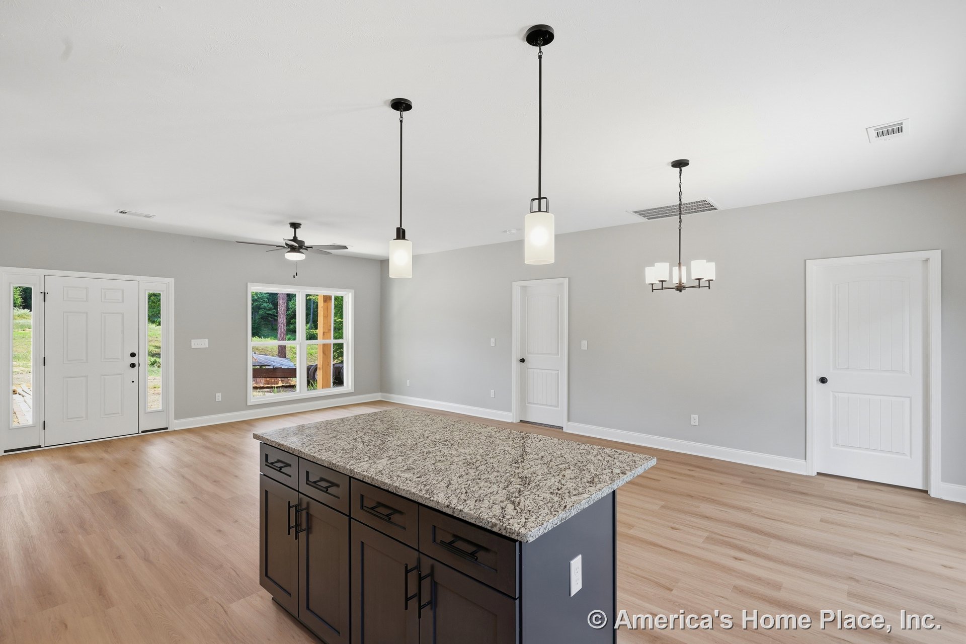 Granite kitchen island with pendant lights, light wood plank flooring, ceiling fan, large front window, white paneled interior doors, neutral wall color, and open floor plan.