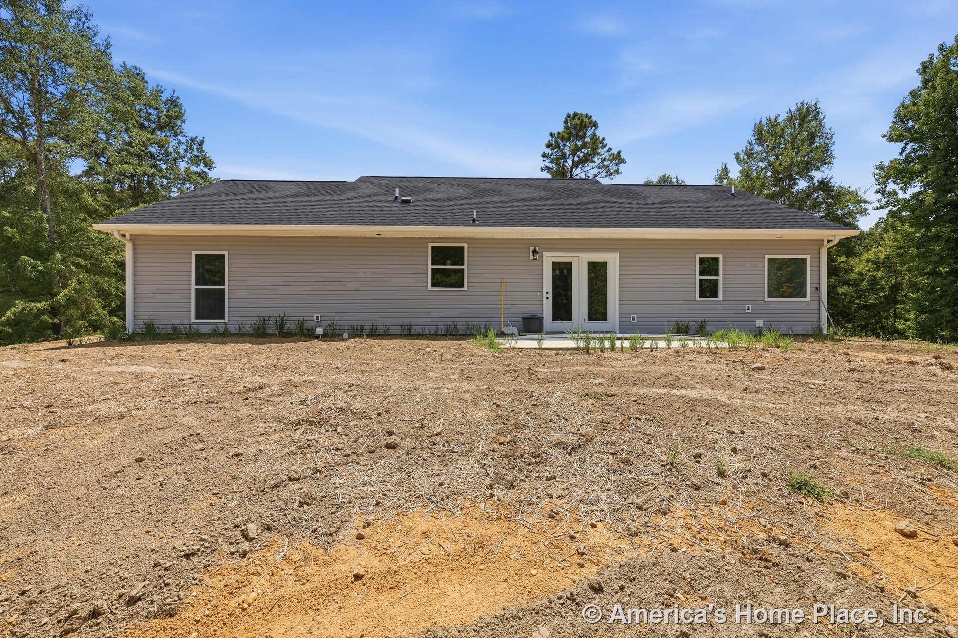 Gray vinyl siding and black shingle roof on single-story home, rear elevation with concrete patio, double glass doors, multiple rectangular windows, exterior lighting fixture, and