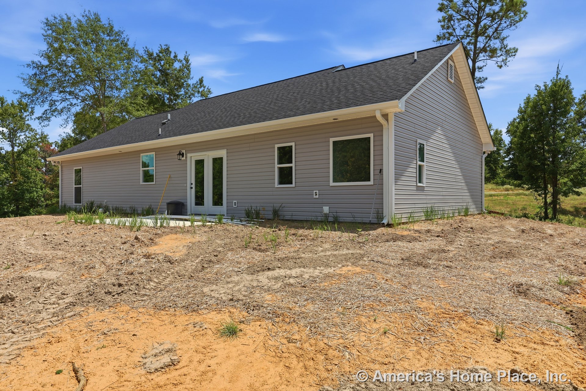 Gray vinyl siding exterior with white trim windows, gable roof, exterior lighting fixture, double glass doors opening to concrete patio.