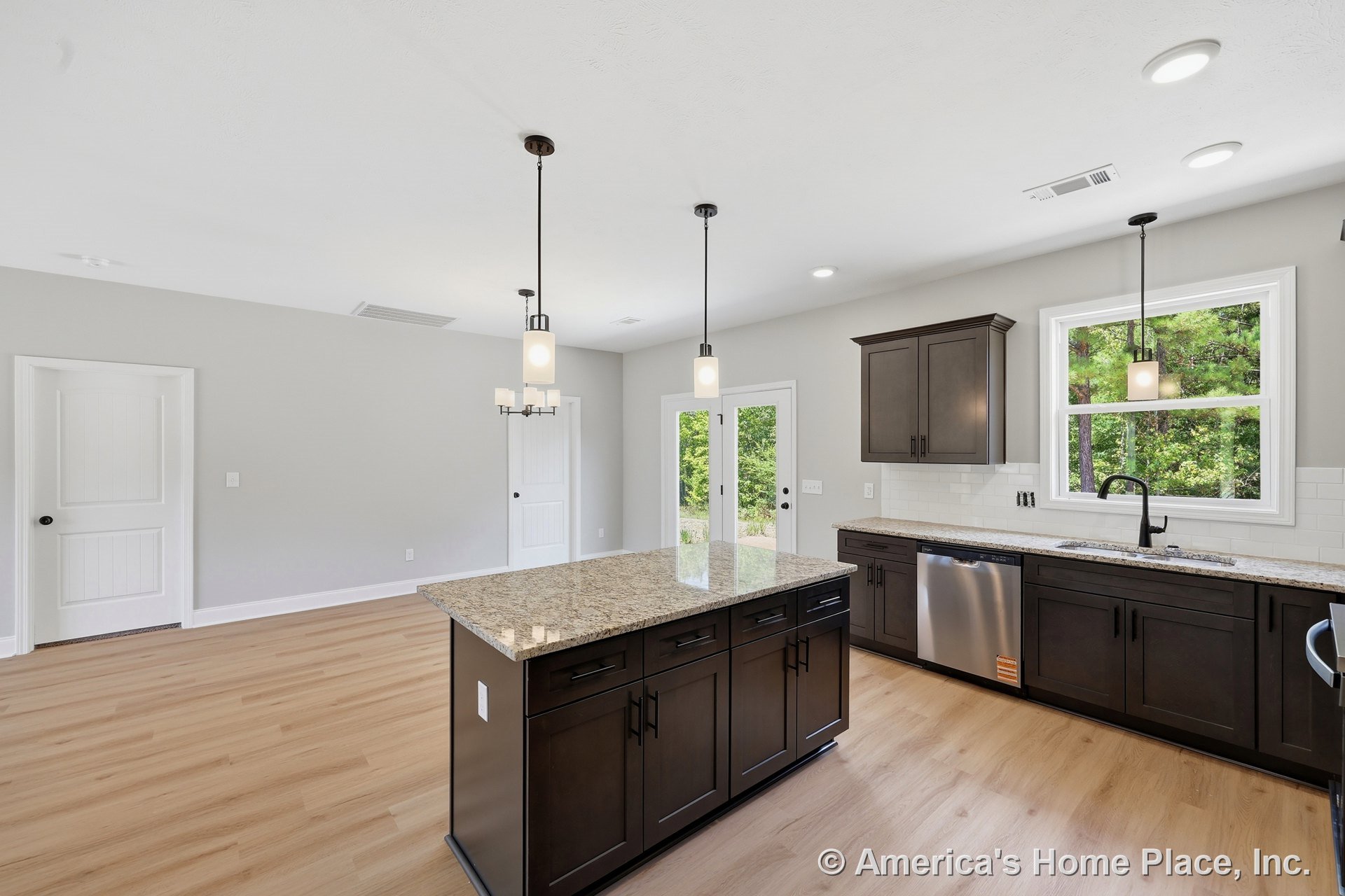 Dark wood kitchen cabinetry with granite countertops, large island with pendant lighting, stainless steel dishwasher, white subway tile backsplash, light wood flooring, double