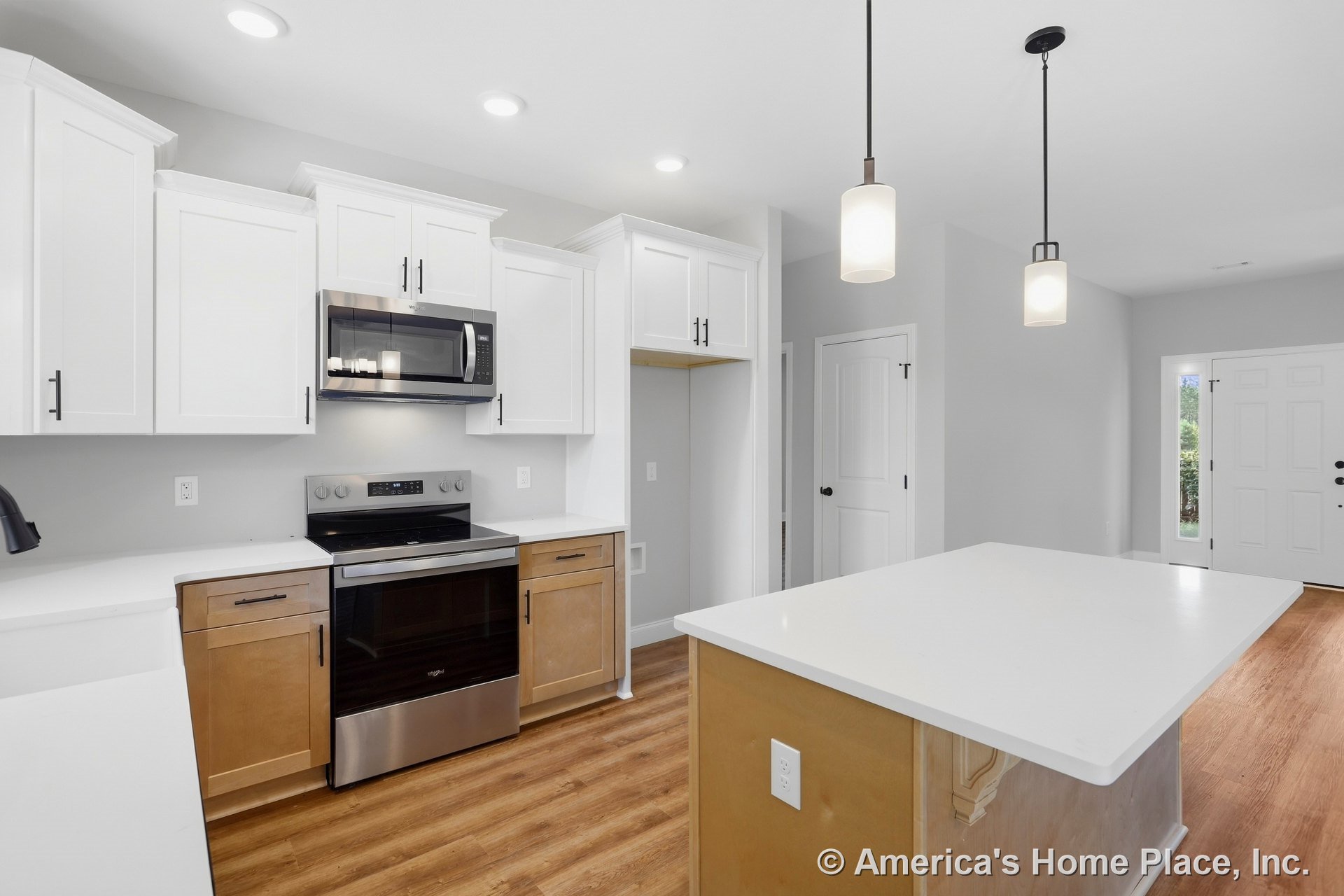 White shaker upper cabinets and wood base cabinetry with quartz countertops, stainless steel appliances, pendant lights above the kitchen island, vinyl plank flooring, recessed
