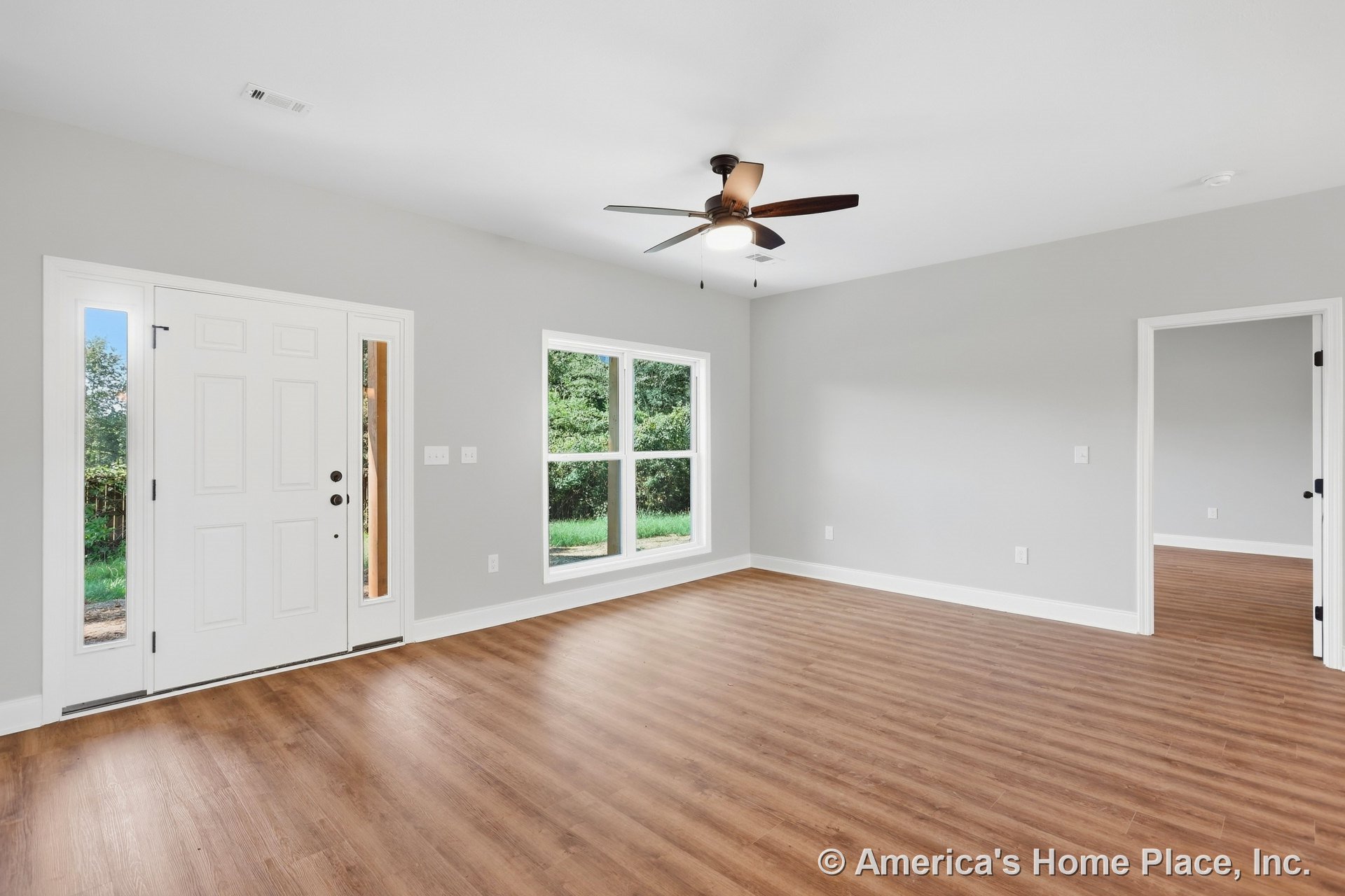 Living room with wood-look vinyl plank flooring, gray painted walls, large double window with white trim, ceiling fan featuring built-in lighting, and wide doorway leading to