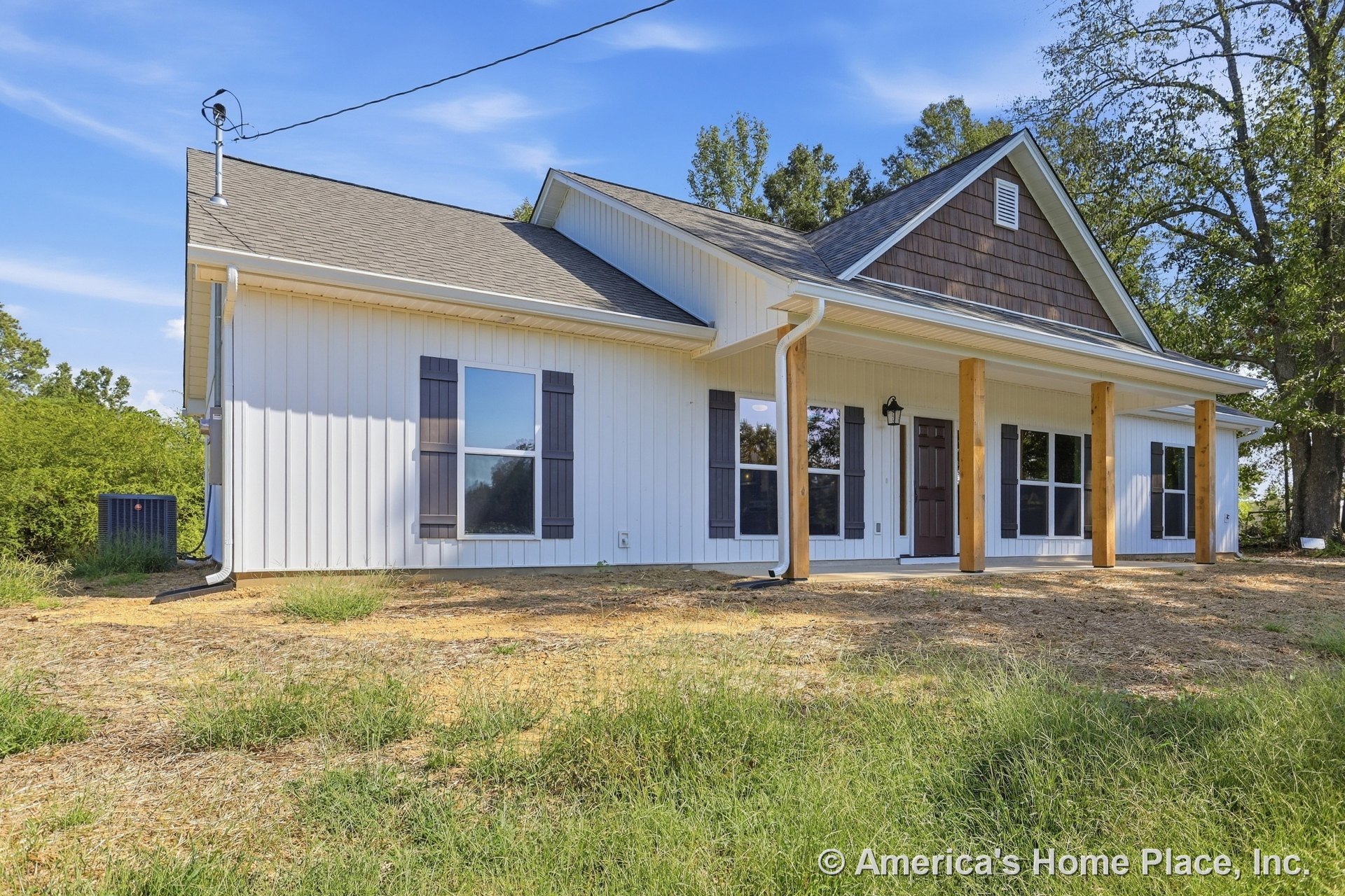 Covered front porch with wood support columns, board-and-batten siding, dark window shutters, gable roof, exterior light fixture, and trim surrounding windows and front door.