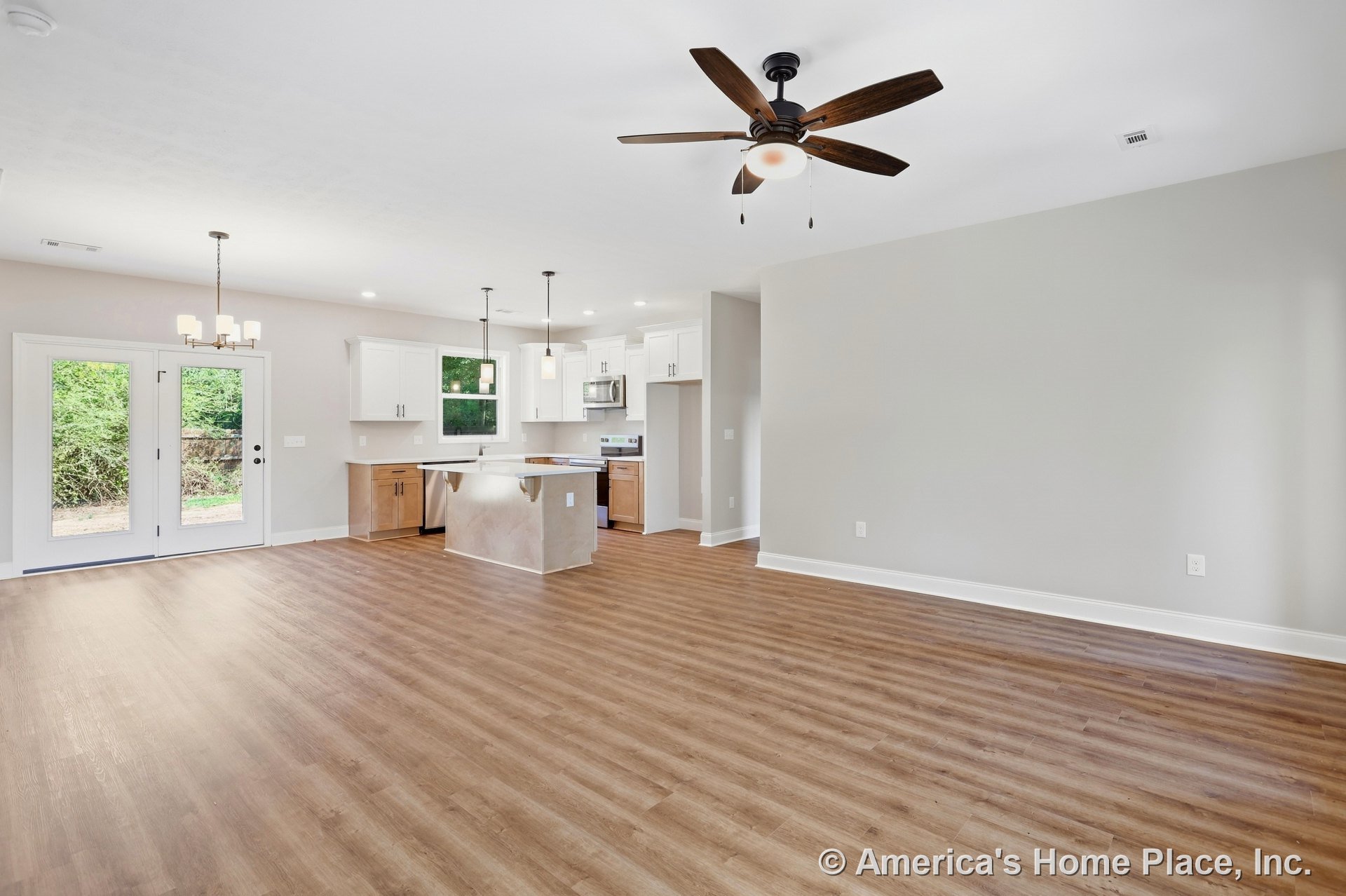 Open-concept living area with wood-look plank flooring, ceiling fan with light, modern kitchen featuring white cabinetry, stainless steel appliances, pendant and chandelier