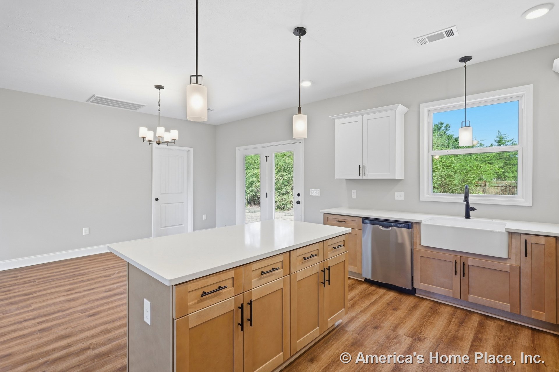 Spacious kitchen with large quartz island, white shaker cabinets, farmhouse sink under window, pendant and recessed lighting, wood-look flooring, stainless steel dishwasher, and