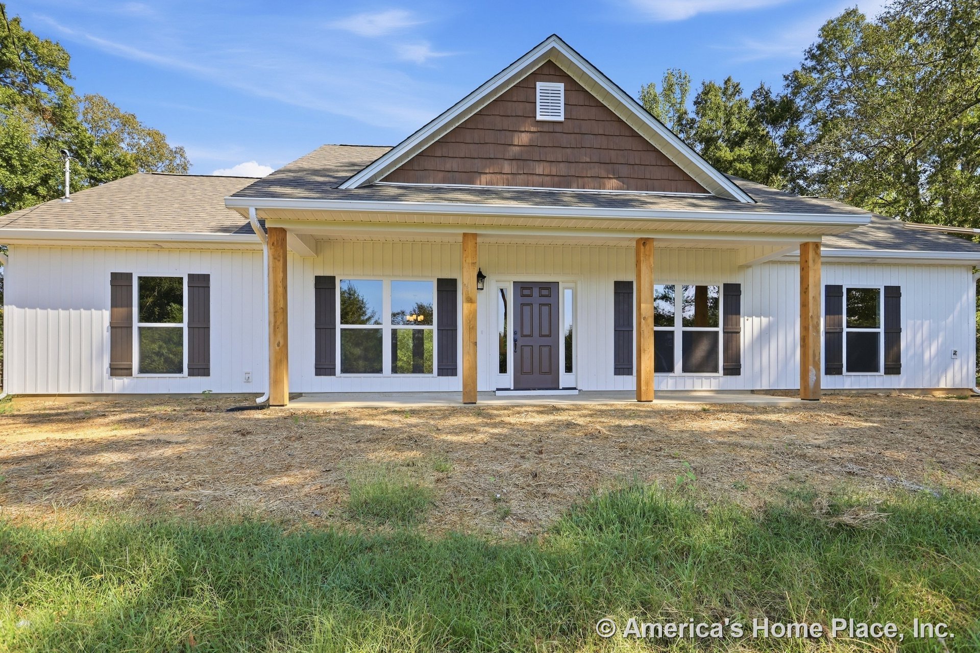 Covered front porch with wooden support columns, multiple large windows with shutters, dark front door, vertical siding, gable roof, decorative trim, and outdoor lighting fixtures.