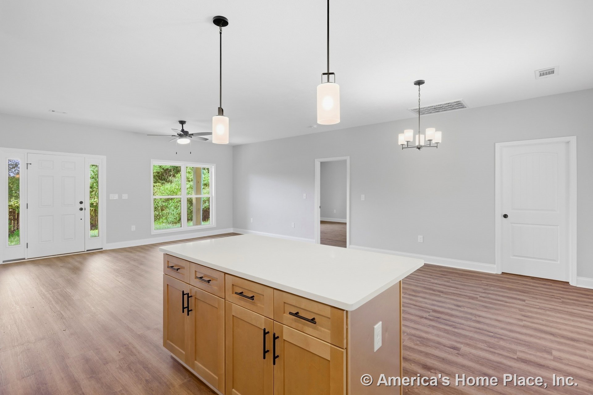 Kitchen island with light wood cabinetry and quartz countertop, open to living area with large double windows, modern chandelier and pendant lights, wood-look flooring, white