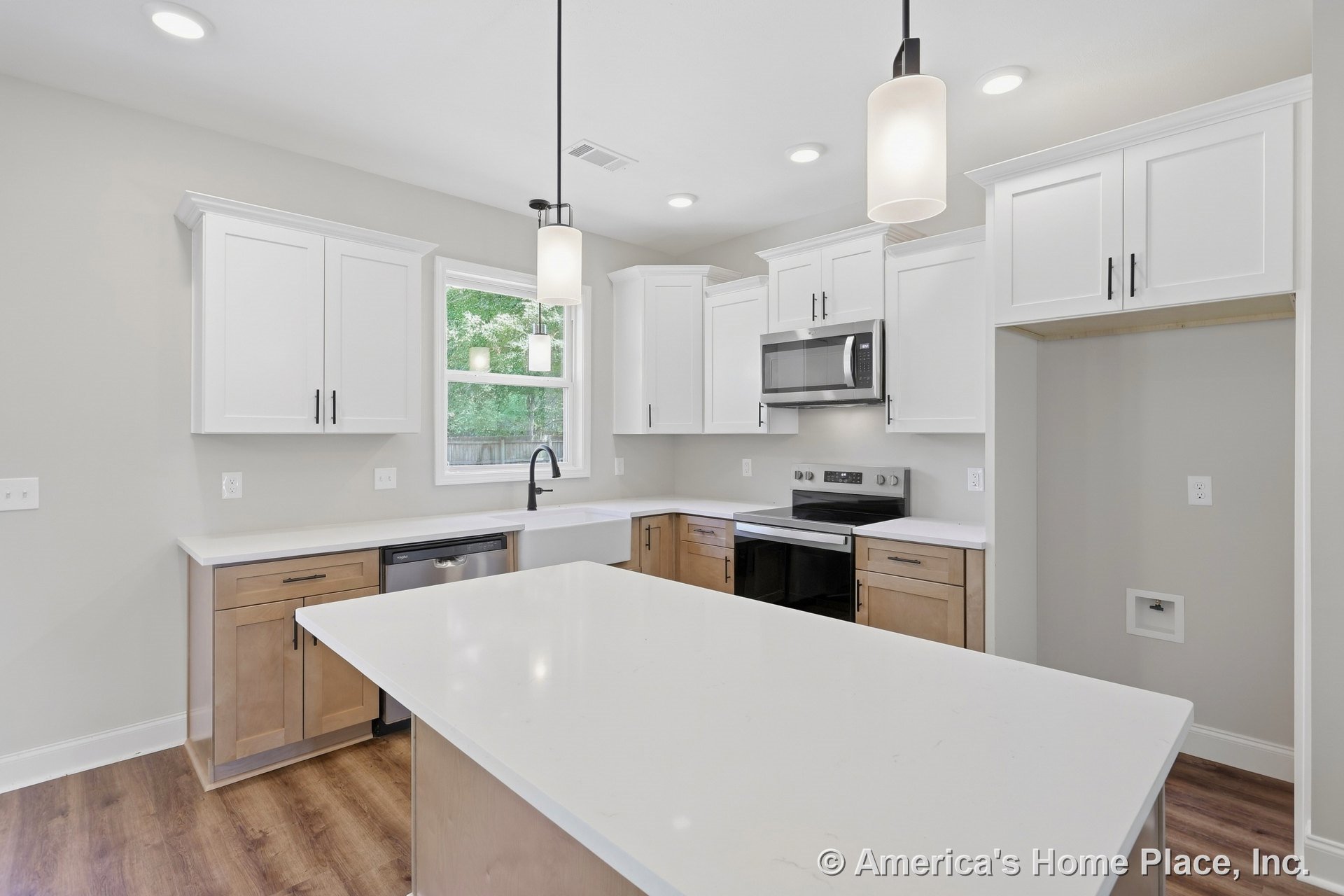 White shaker upper cabinets and wood base cabinetry with quartz island countertop, stainless steel microwave and oven, pendant and recessed lighting, farmhouse sink beneath window