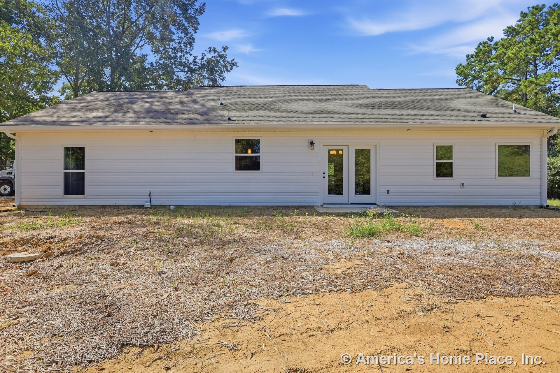 White vinyl siding and shingle roof with multiple rectangular windows, double glass door entry, exterior wall lighting, and unfinished backyard.