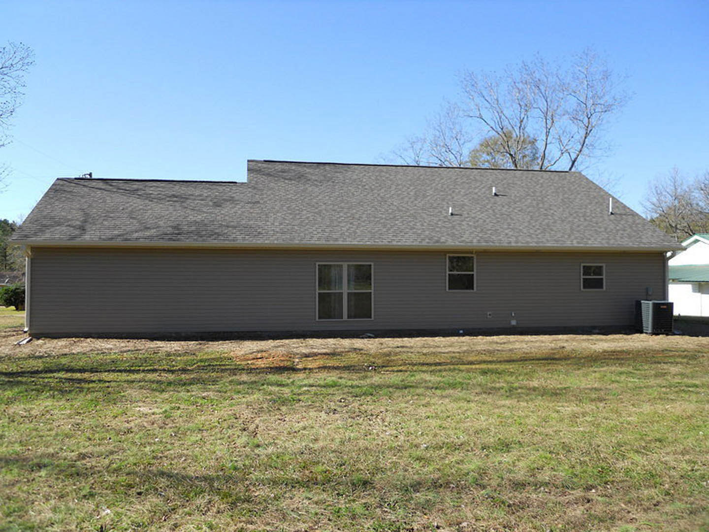 Two-story home with white-framed windows, gray siding, and gabled roof, surrounded by green grass and mature trees