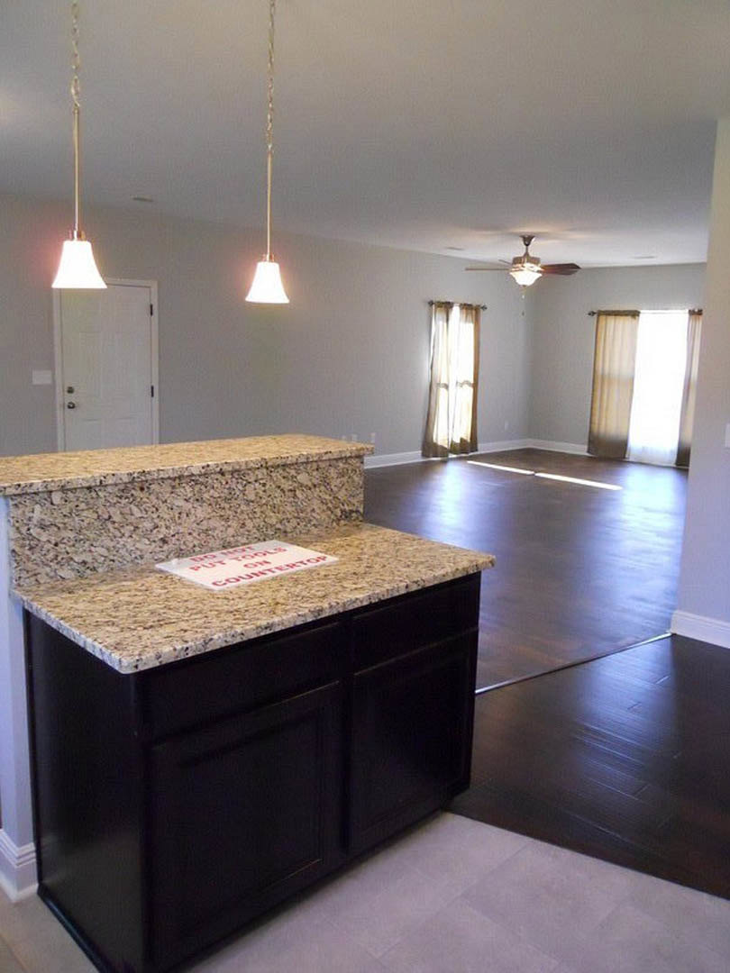 Marble countertop kitchen with white cabinetry, stainless steel sink, tile backsplash, and light wood flooring