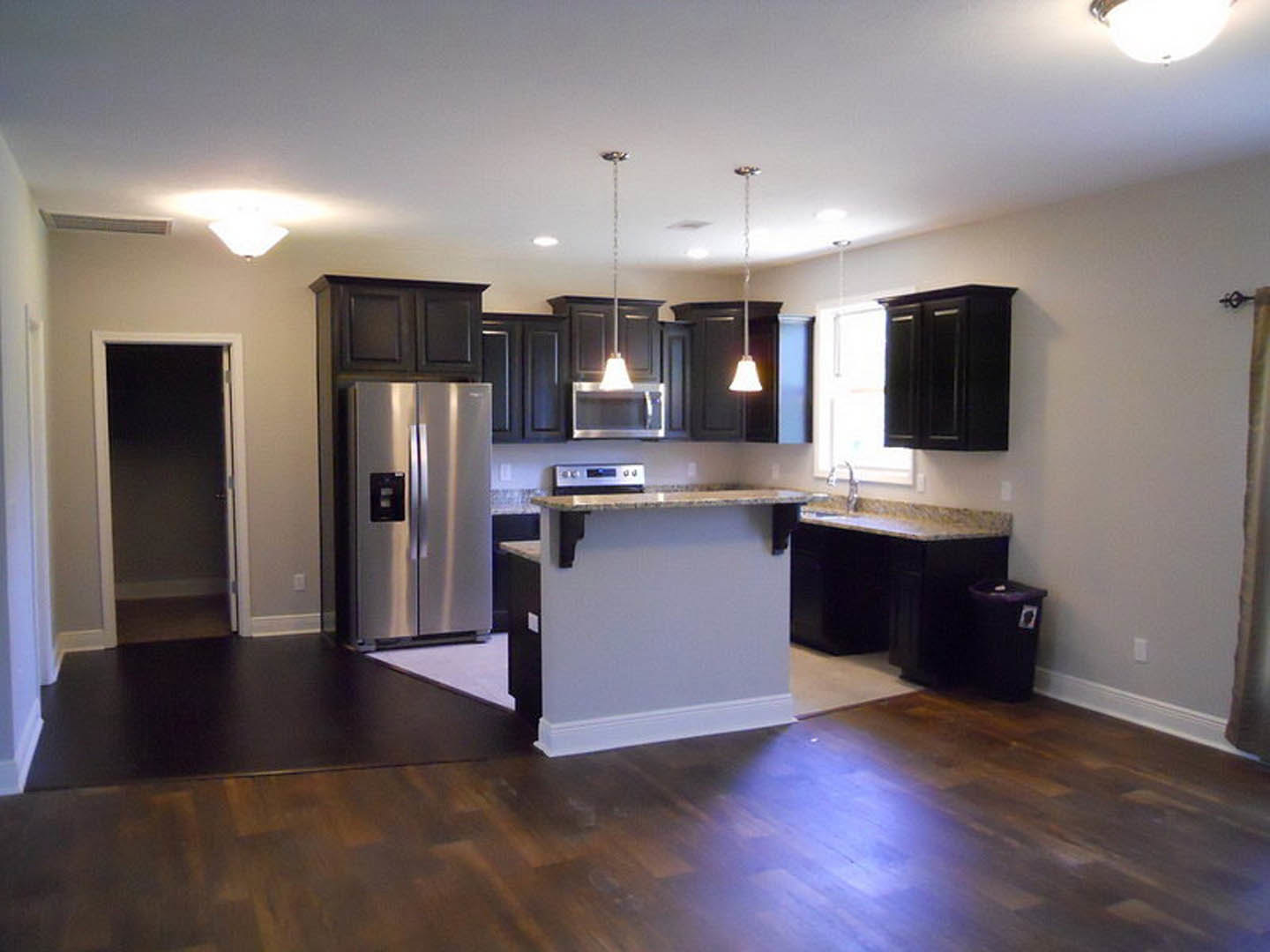 Kitchen with stainless steel refrigerator, wood flooring, marble countertop, white cabinetry, and black trash can with sticker
