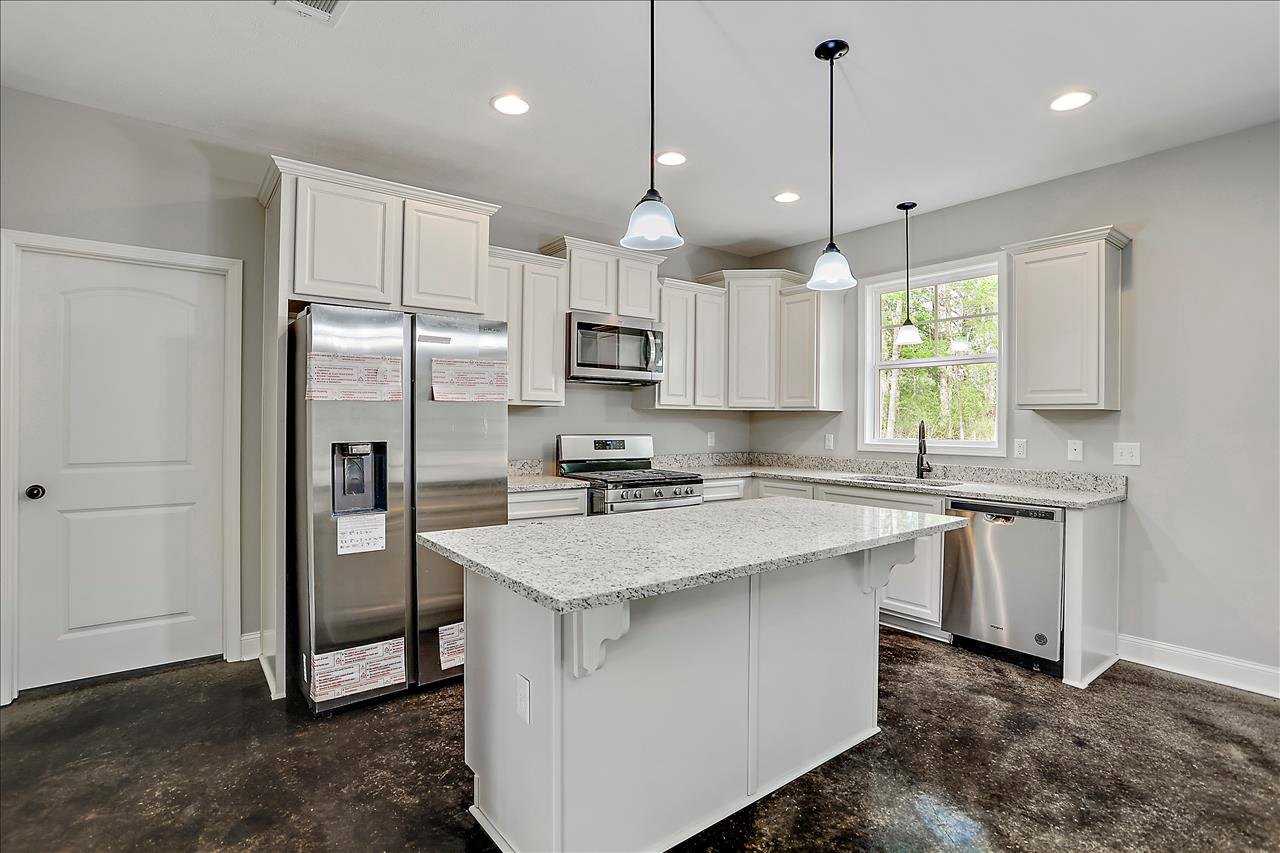 White kitchen with shaker cabinets, large central island featuring granite countertop, stainless steel stove and microwave, built-in water dispenser, white door with black handle