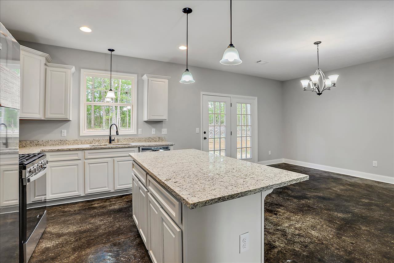 Spacious kitchen featuring a large marble-topped island, white cabinetry, stainless steel sink beneath a window, chandelier with white shades, and light wood flooring