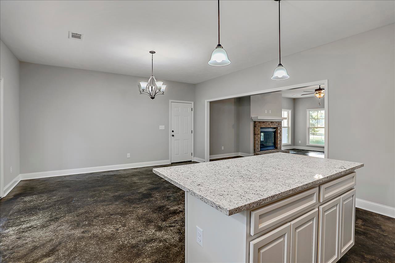 Open-concept kitchen and living room featuring a granite island with white cabinetry, tile backsplash, brick fireplace, white door with black knobs, chandelier with white shade