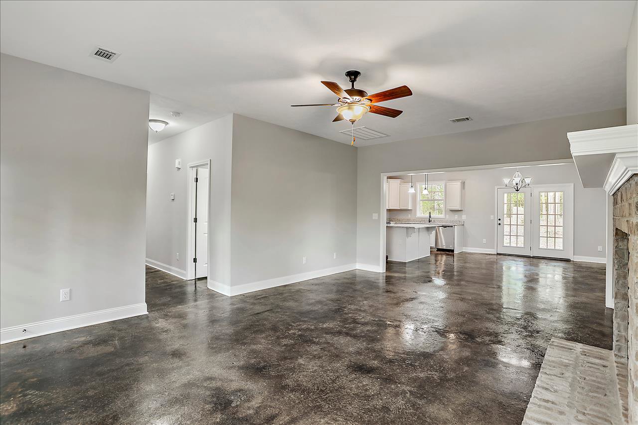 Spacious open-plan room featuring a ceiling fan with light fixture, white walls, concrete flooring, adjacent kitchen area, and white double doors with glass panes.