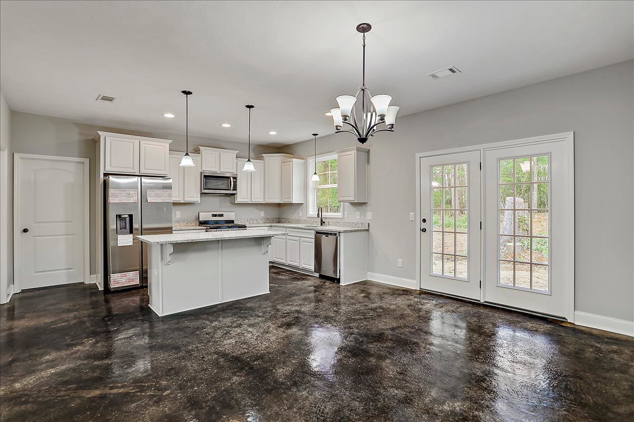 White kitchen with shaker cabinets, marble countertop, stainless refrigerator with open door, built-in microwave, black hardware, and double doors with glass panes.