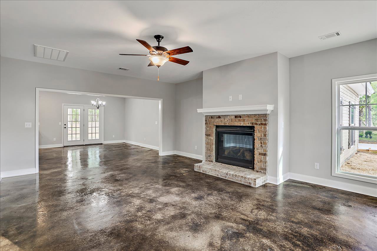 Living room featuring a glass door fireplace, ceiling fan with light fixture, concrete flooring, double glass-paneled doors, and window overlooking neighboring house