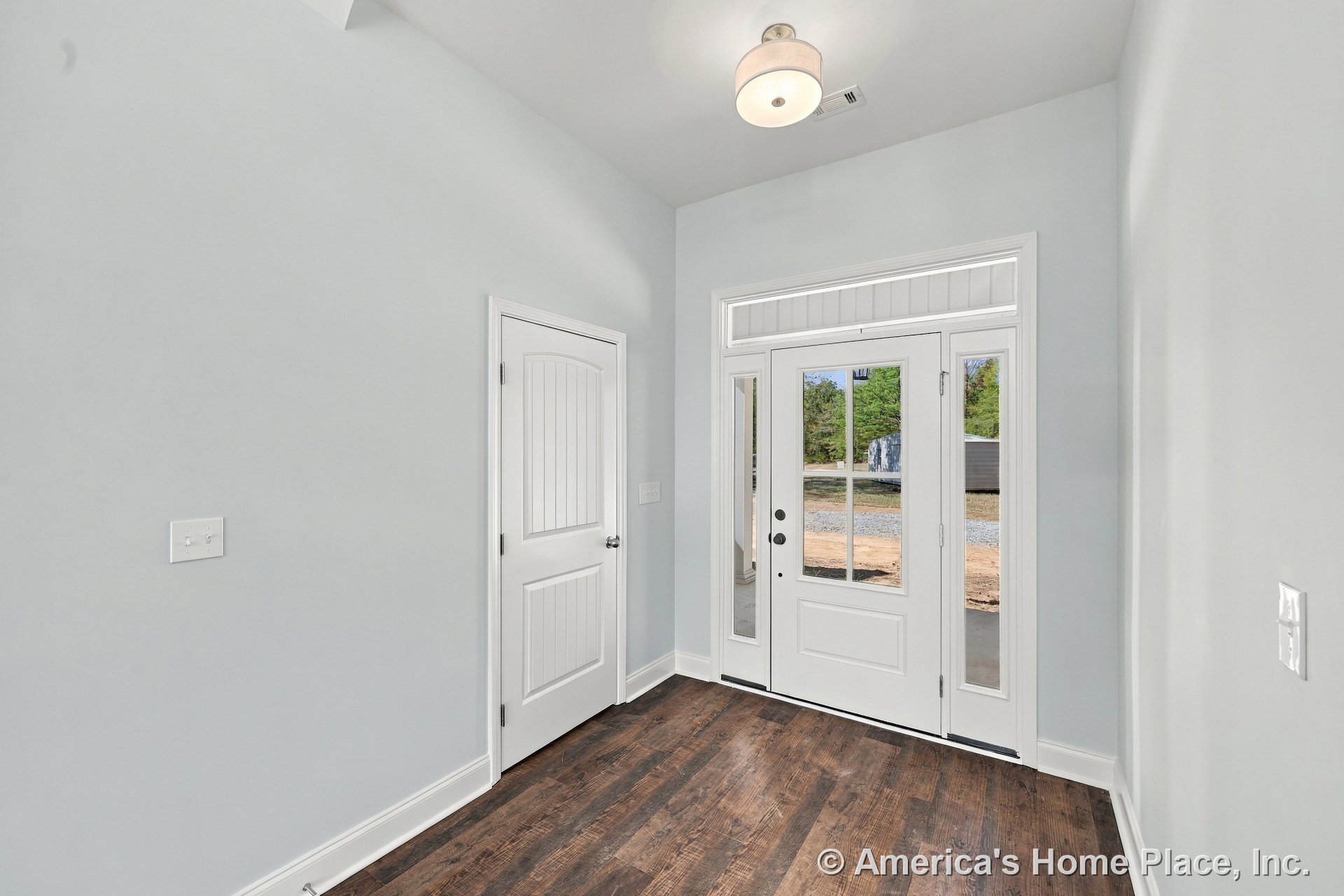 White paneled front door with sidelights and transom window, dark wood flooring, light gray walls, white interior door, flush mount ceiling light, white trim and baseboards, modern