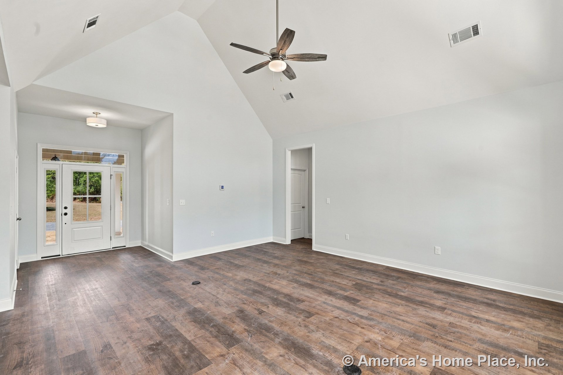 Living room with vaulted ceiling, wood-look plank flooring, ceiling fan with light, white trim and baseboards, entry door topped by transom window, recessed lighting, and abundant