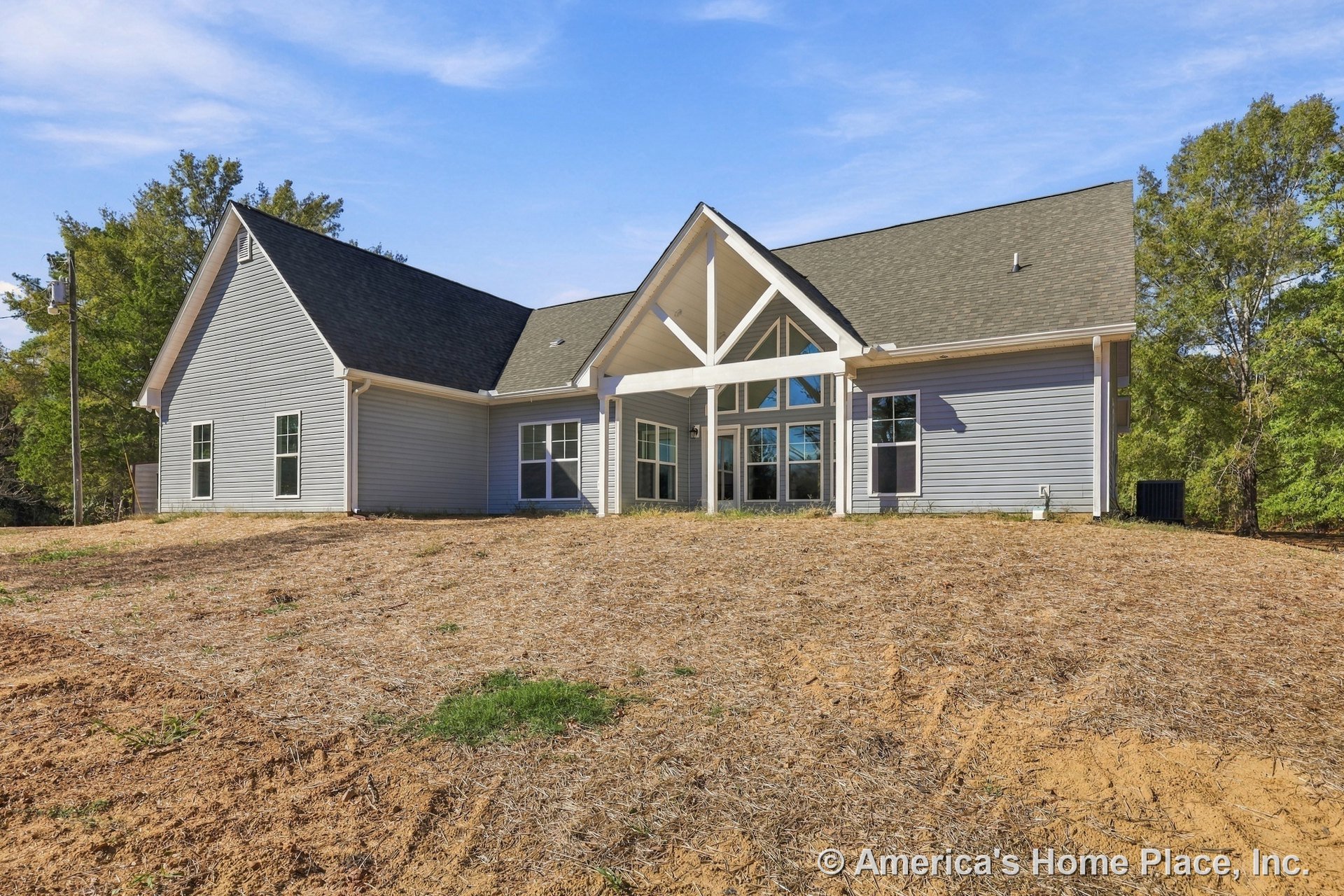 Rear exterior of modern farmhouse with high gabled roof, exposed truss beams, gray horizontal siding, multiple large rectangular windows, covered porch, and white trim accents.