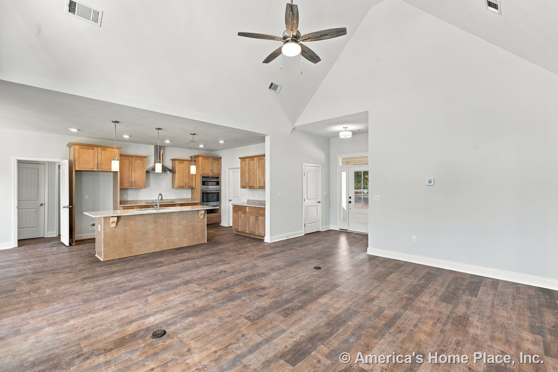 Open concept living area with vaulted ceiling and ceiling fan, wood-look plank flooring, kitchen island with sink, natural wood cabinetry, granite countertops, pendant and recessed