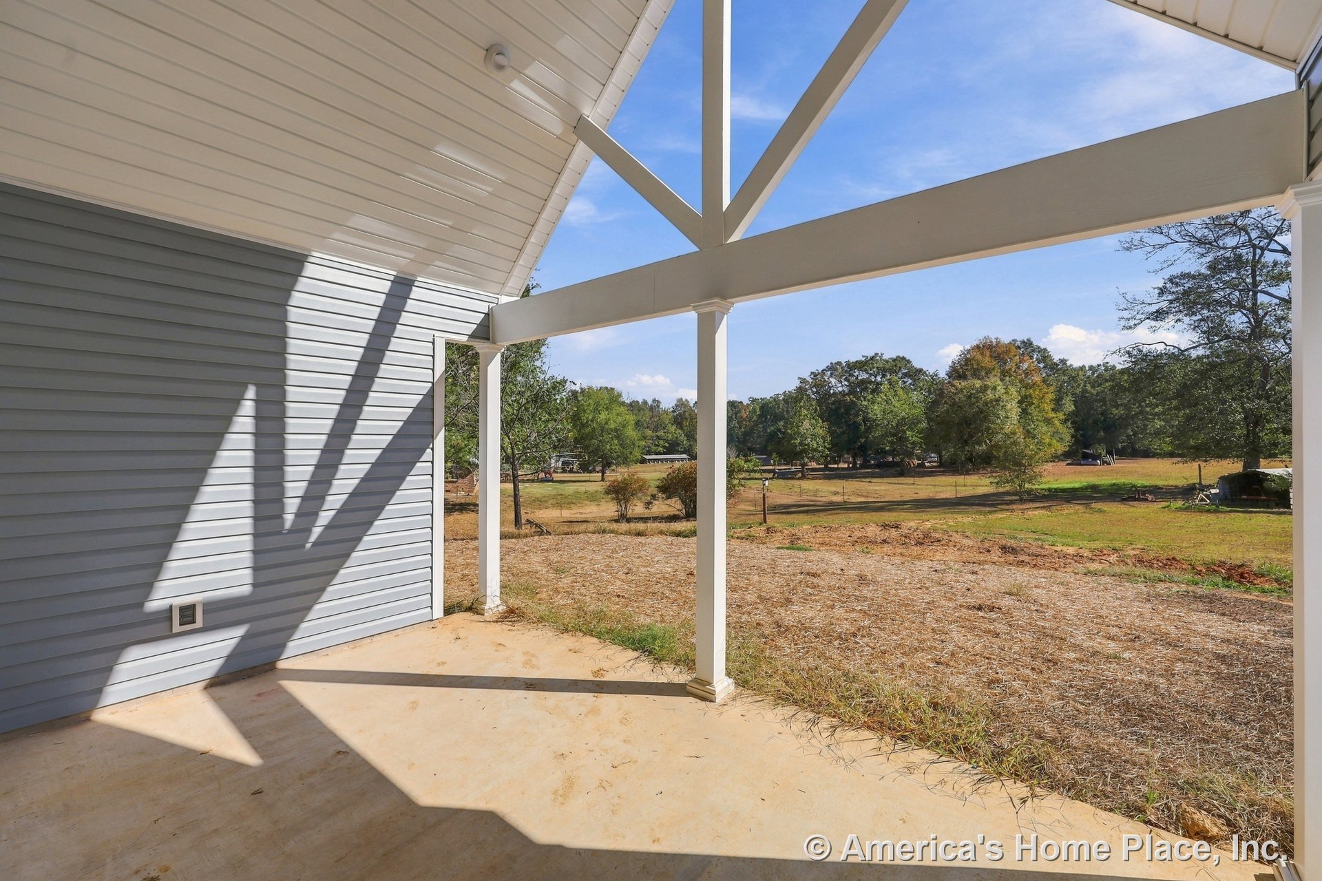 Covered porch with white structural beams and columns, concrete flooring, vinyl siding exterior, and open yard view.