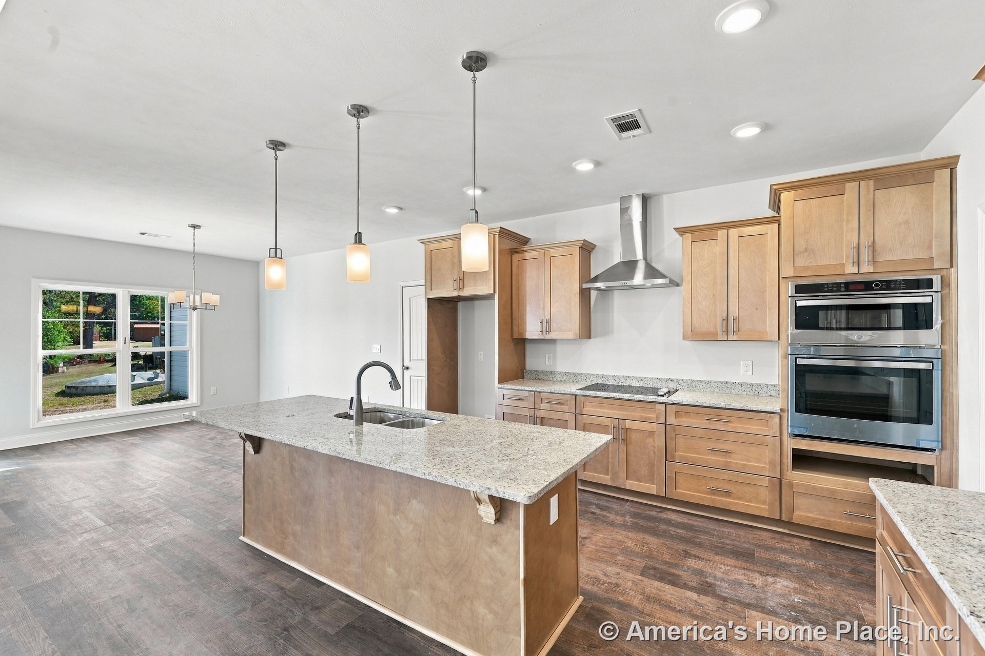 Light wood cabinetry and granite countertops surround a spacious kitchen island with built-in sink, pendant lighting fixtures overhead, double wall oven, stainless steel range
