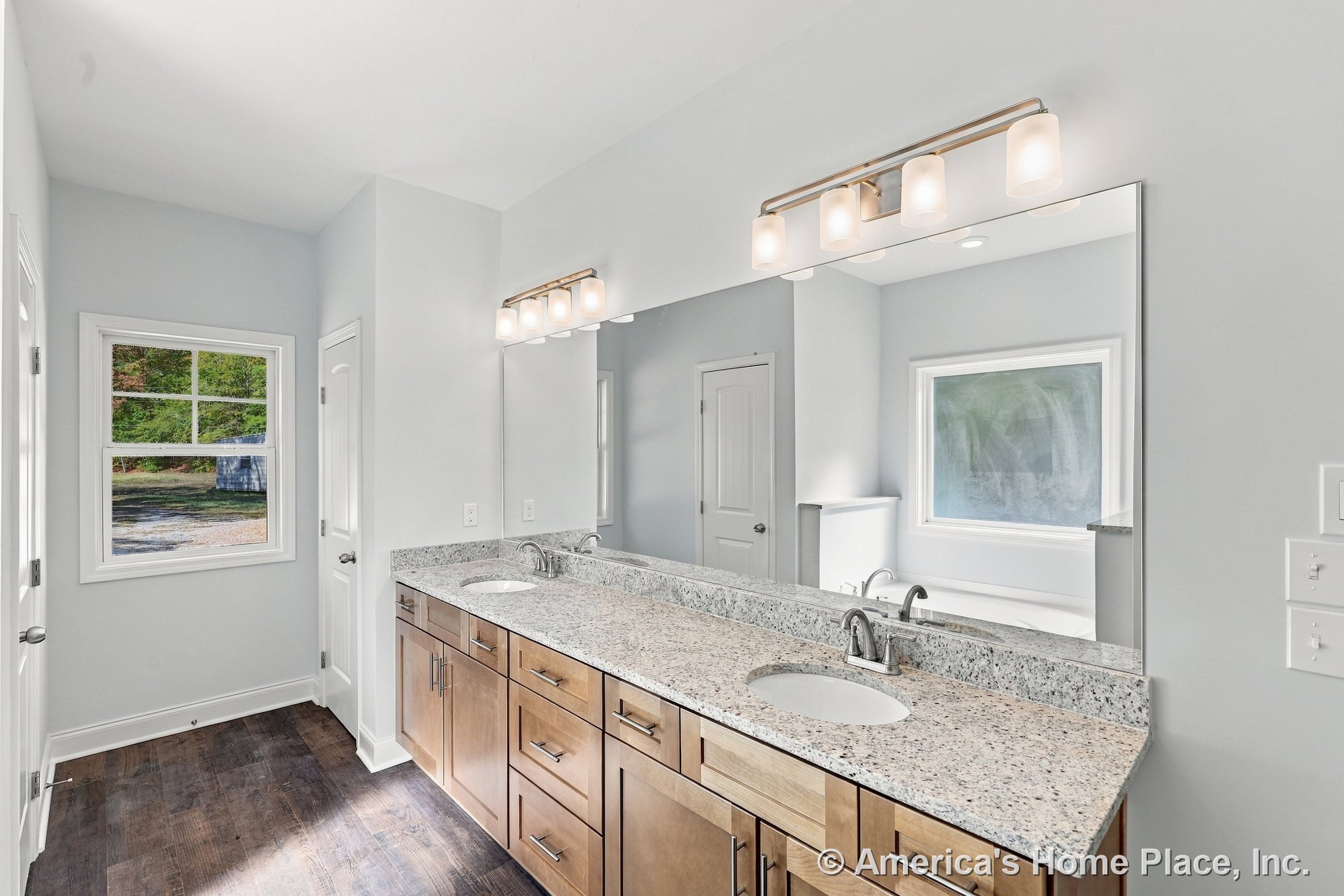 Double sink vanity with granite countertop and wood cabinets, large wall mirror, built-in vanity lighting, white trim window, neutral walls, modern fixtures, and tile flooring.