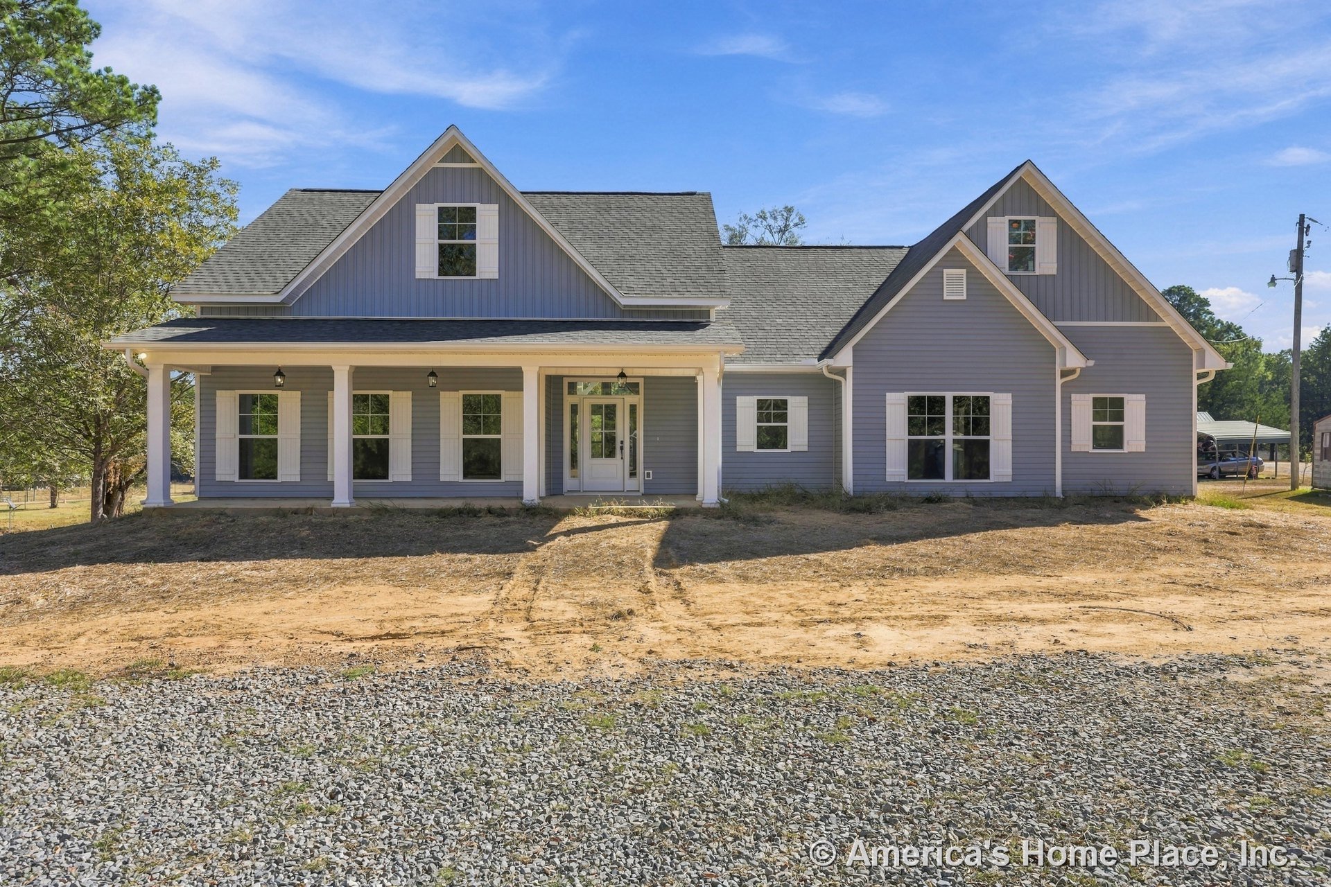 Large covered front porch with white columns, gray siding exterior, multiple windows with white shutters, gable roof, and prominent entry door.