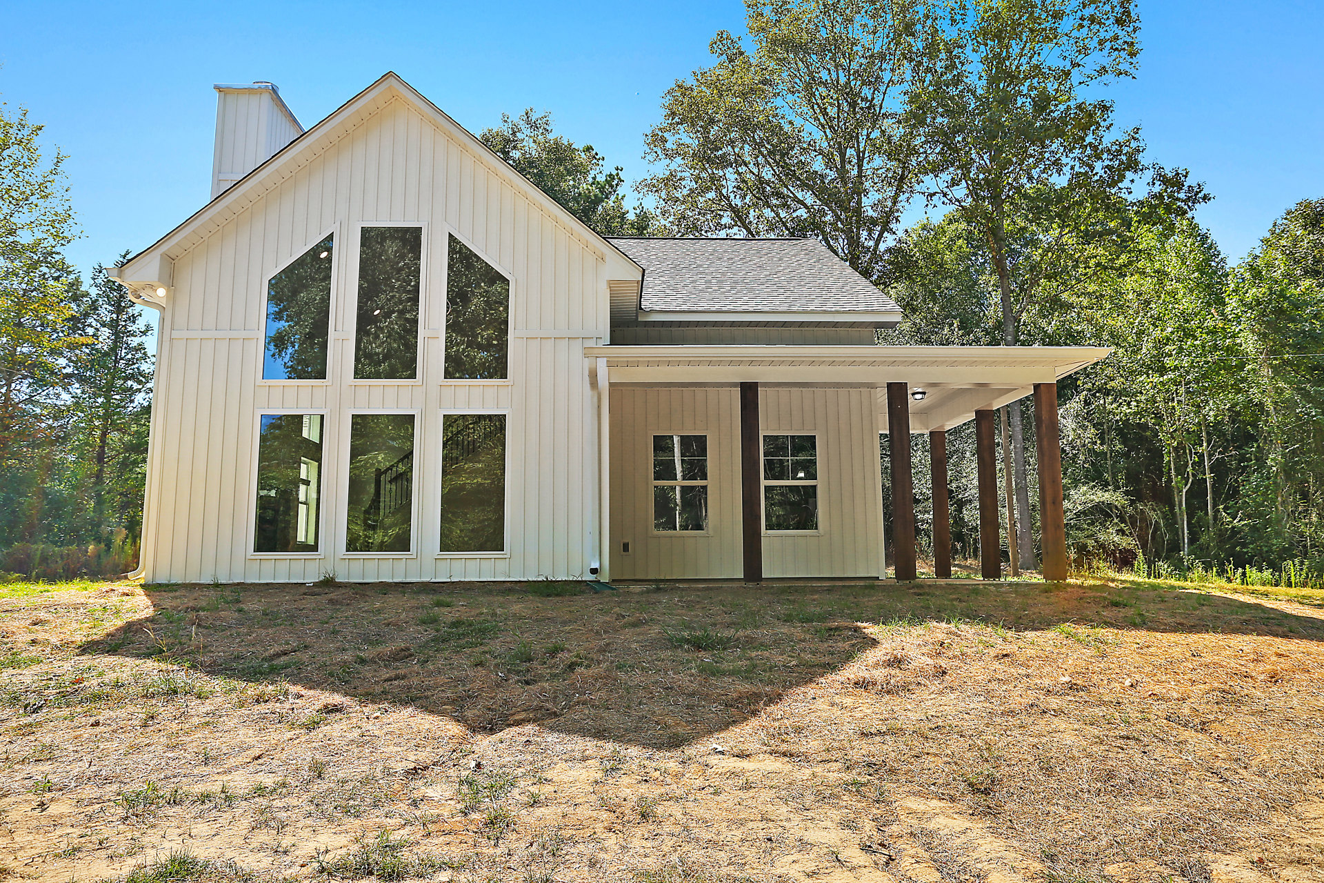 White house with wide front porch, white pillars, large windows, and mature trees in the background