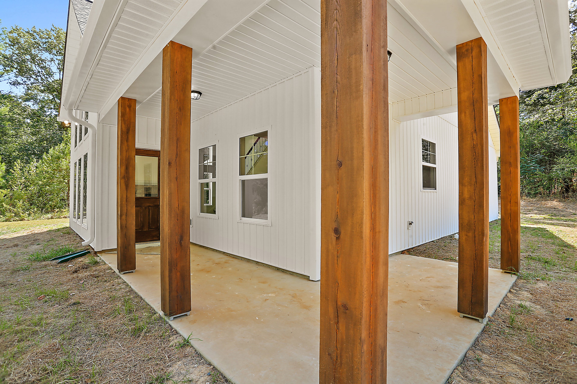 White exterior home with natural wood pillars, large windows reflecting trees, and white railing along entry steps