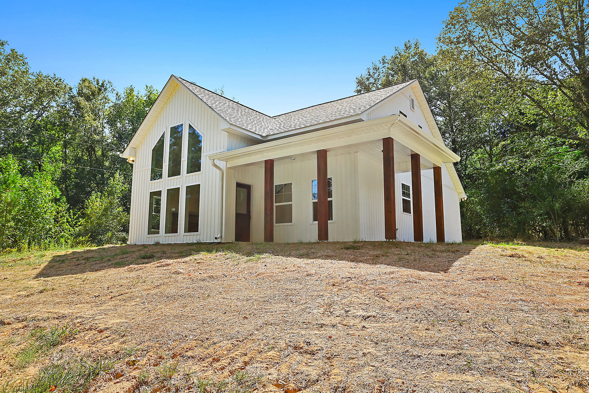 White house with brown pillars, expansive front porch, multiple grid windows, brown mulch landscaping, blue sky in background