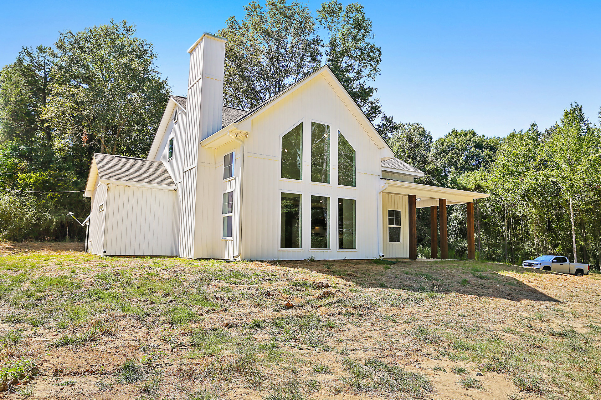 White cottage-style home with tall brick chimney, large windows, and surrounding trees on a grassy lawn
