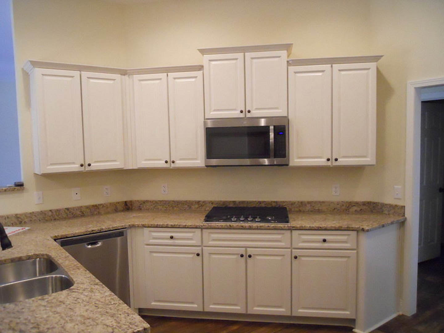 White kitchen cabinets with granite countertops, stainless steel sink and dishwasher, built-in microwave, and drawers, with a close-up of cabinetry and a blurred black object in