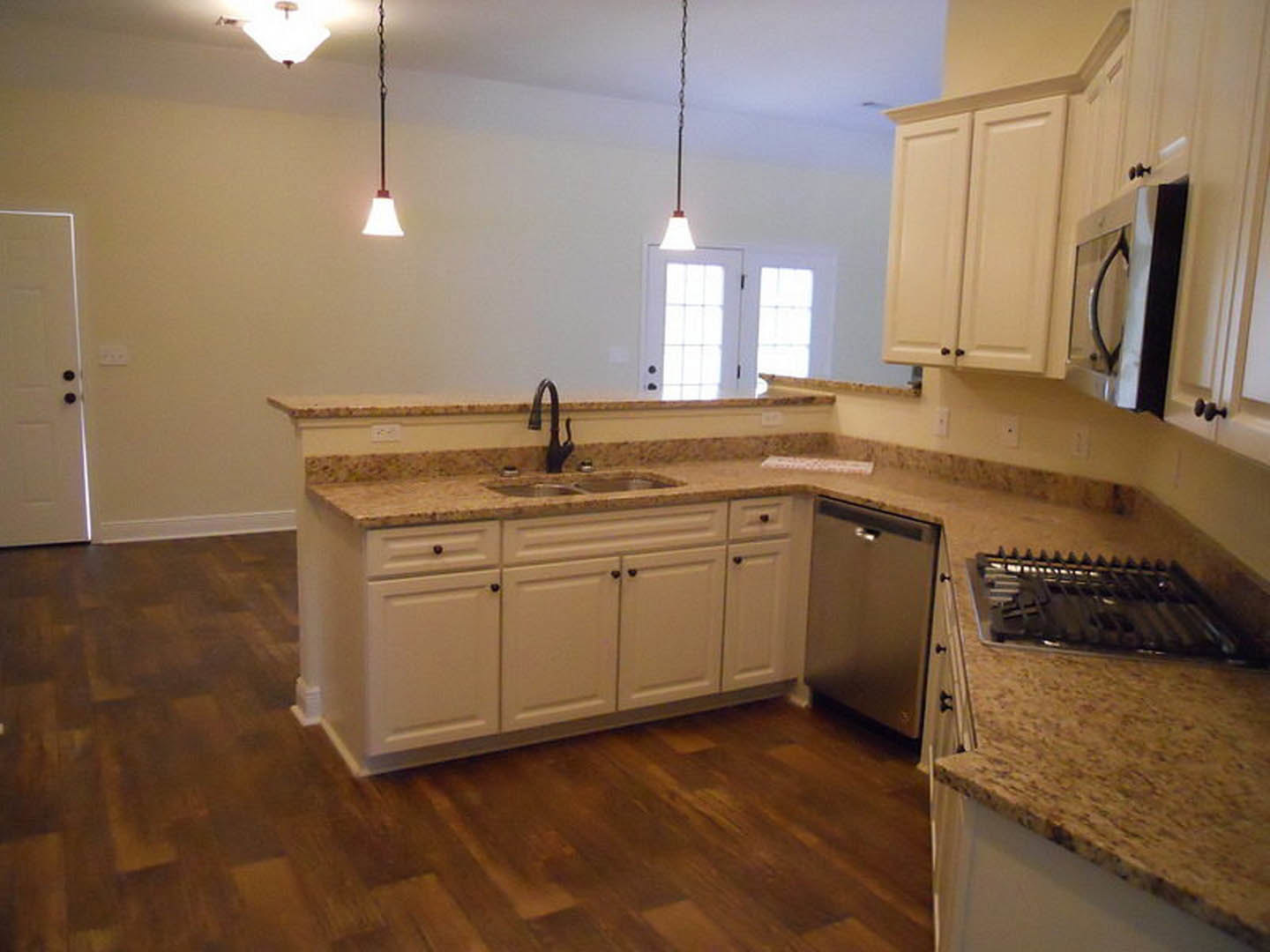 Granite countertops with white cabinetry, stainless steel sink and faucet, light-colored walls, and hardwood flooring in a modern kitchen