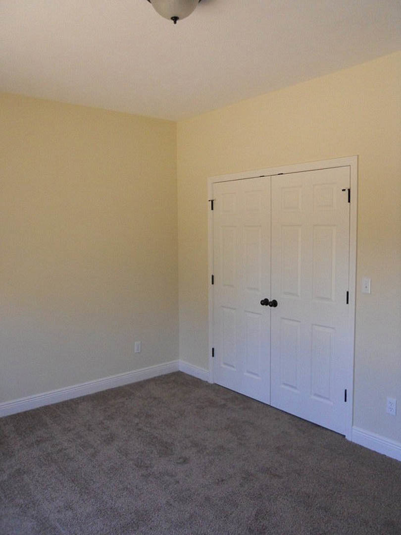 Carpeted room featuring two white doors with black knobs, white walls, ceiling light fixture, and plaster finishes.