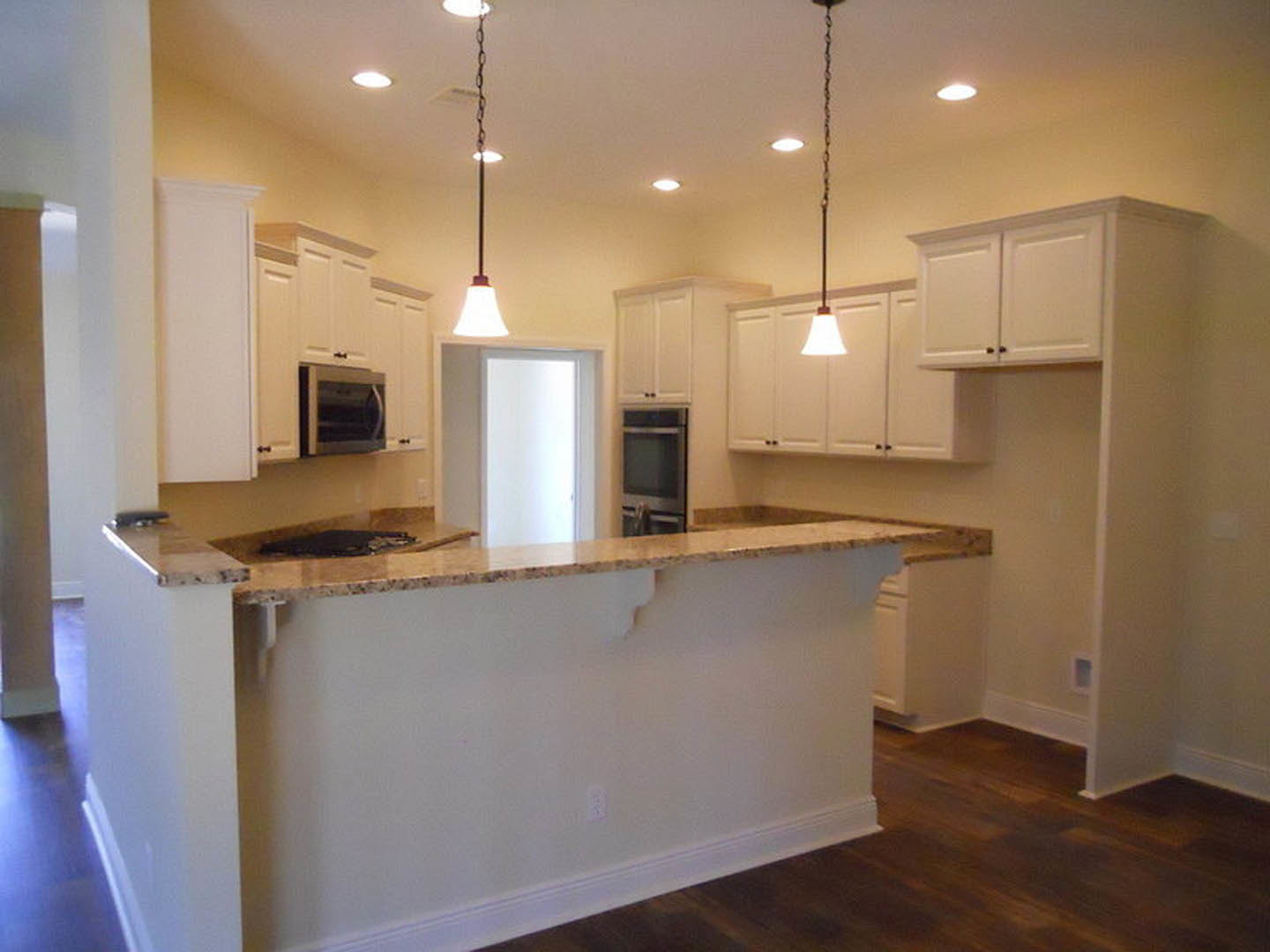 White kitchen cabinets, marble countertop, stainless steel sink, open microwave door, tiled floor, white walls, recessed lighting