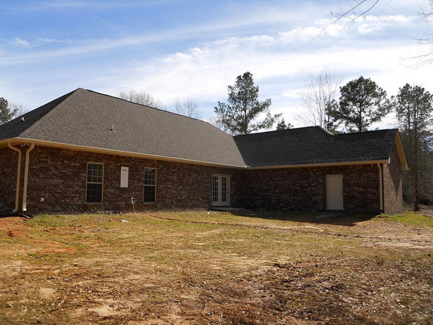 Red brick house with white-trimmed windows, black-bordered front door, grassy yard, mature tree, and partly cloudy sky