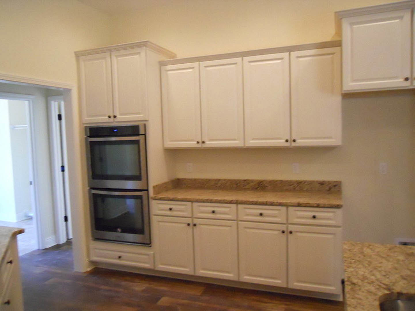 White kitchen cabinets with black knobs, granite countertops, stainless steel refrigerator, bowl on counter, white door in background, hardwood flooring