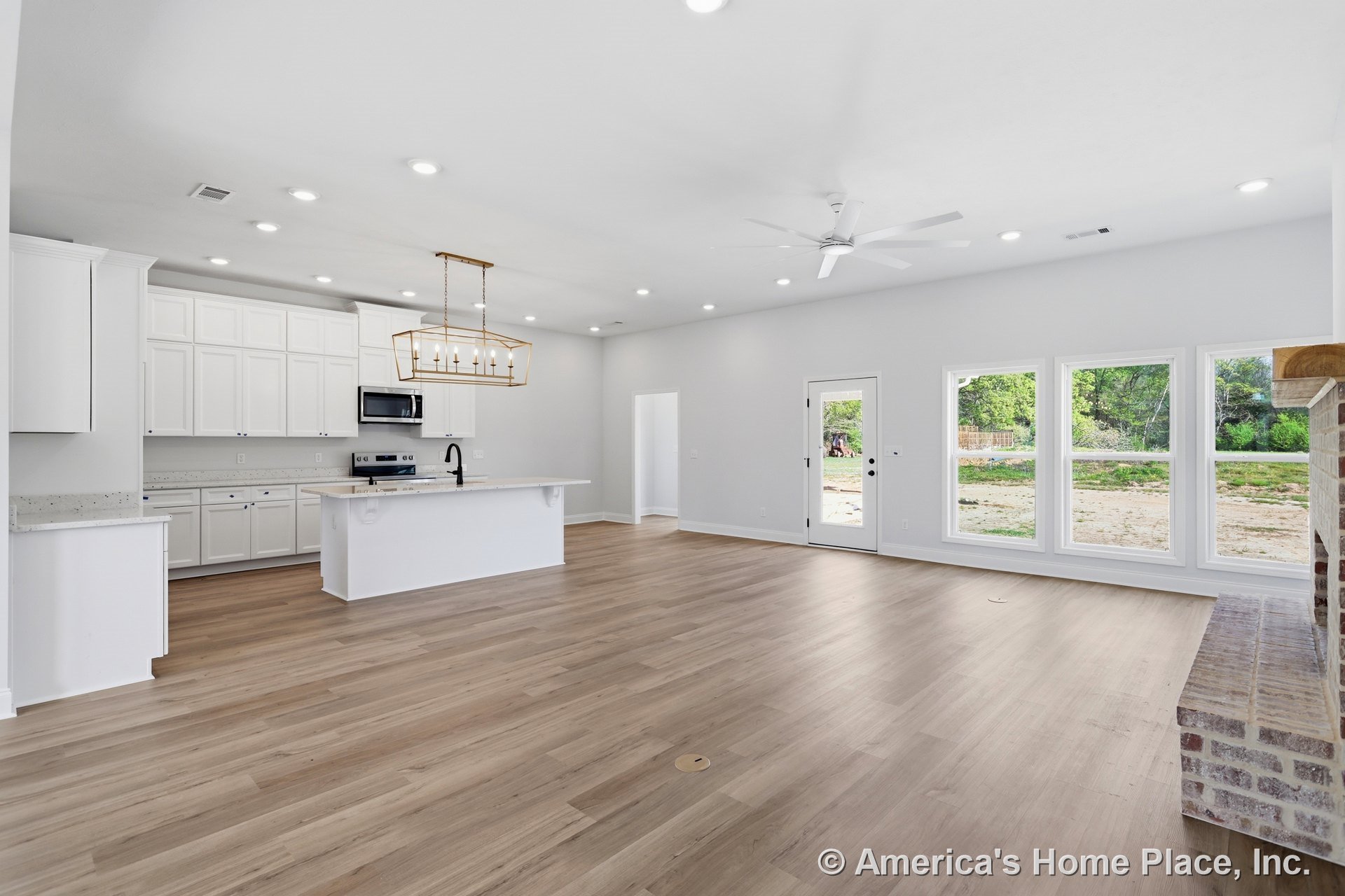 Spacious white kitchen with wood flooring, white cabinetry, black faucet on white countertop, built-in microwave, ceiling chandelier, door opening to grassy yard with tractor