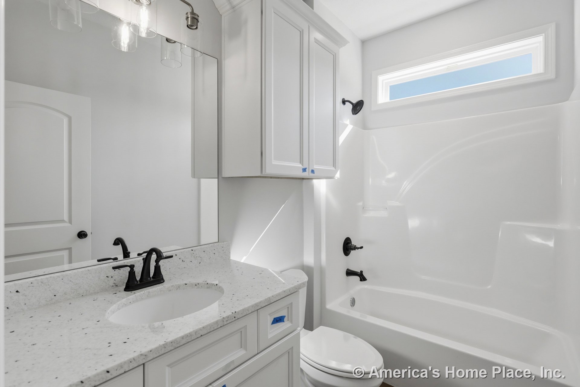 Bathroom with white cabinets, white sink with black faucet, white toilet, and white bathtub; light tile flooring and neutral walls.