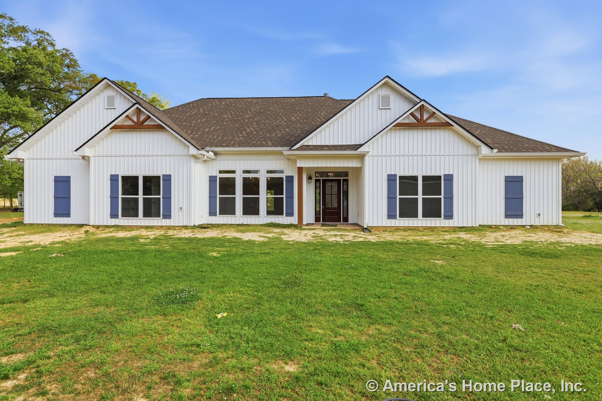 White siding house with brown roof, brown glass-paneled front door, blue shutters, white-framed windows, and green lawn under partly cloudy sky